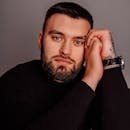 Portrait of a bearded man resting his head on hands, showcasing a thoughtful expression in a studio setting.