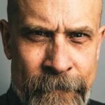 Close-up portrait of a serious bald man with a beard, conveying intensity and thoughtfulness.