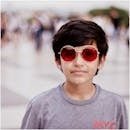 A young boy with stylish red sunglasses stands outside, showing a confident expression.
