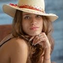 Portrait of a woman with brown hair adorned in a fashionable sun hat indoors.