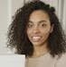 Confident woman with curly hair smiling amidst packages, symbolizing entrepreneurial success.