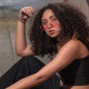 A fashionable woman posing with curly hair and stylish sunglasses, exuding confidence.
